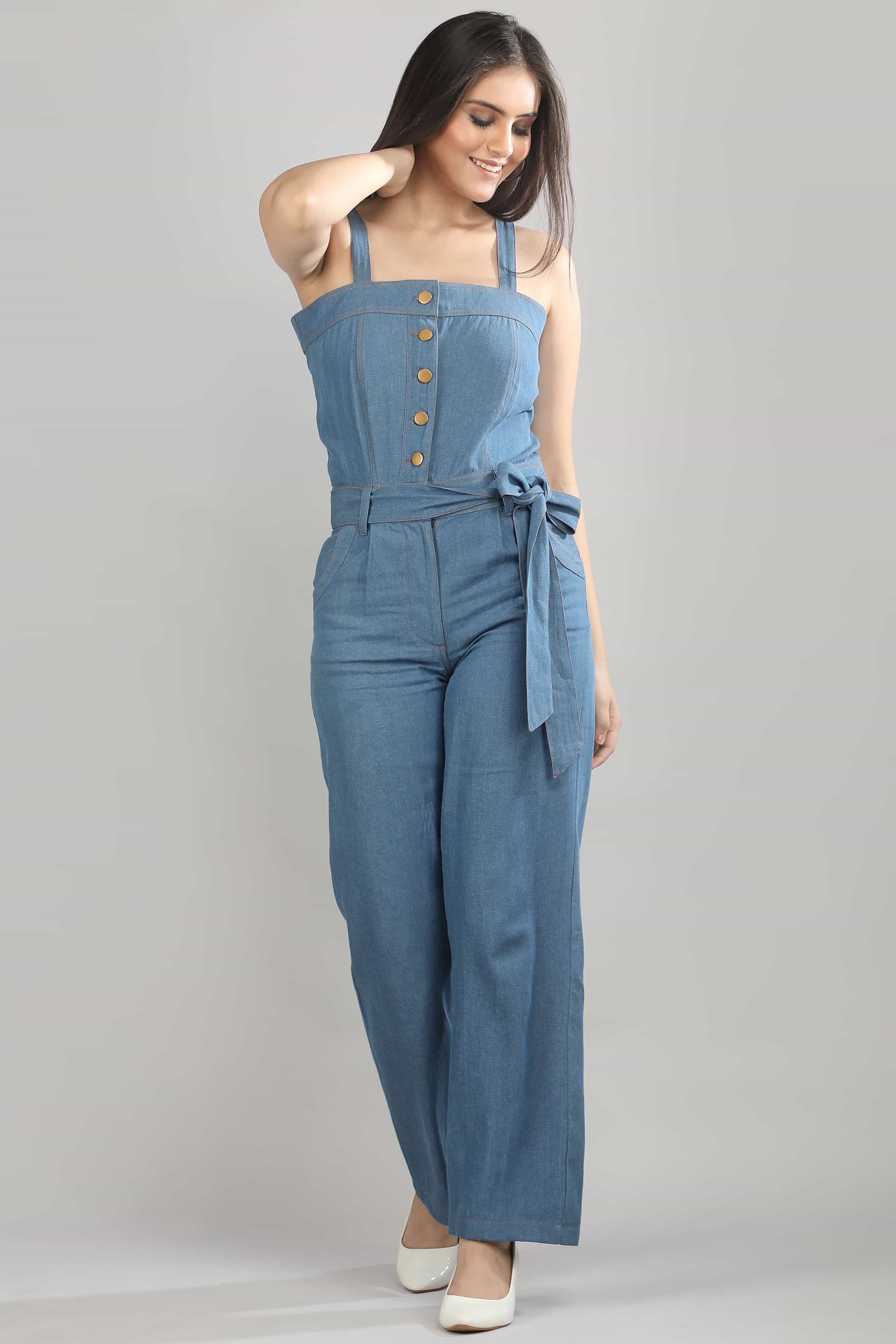 [blue] Angled view of the Caught in Denim jumpsuit by Guilt & Class, highlighting the defined bodice and fluid wide-leg trousers.