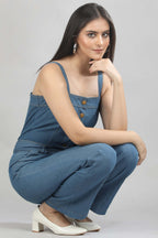 [blue] A model squatting in the Caught in Denim jumpsuit by Guilt & Class, highlighting the comfortable fit and ease of movement in lightweight cotton denim.