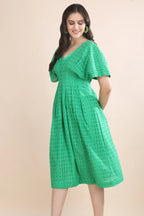 Side profile of a woman modeling the green schiffli midi dress, demonstrating the flattering A-line drape and structured sleeve details.