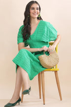 A smiling woman seated in the vibrant green eyelet dress, showcasing the comfortable, breathable fit designed for everyday luxury.