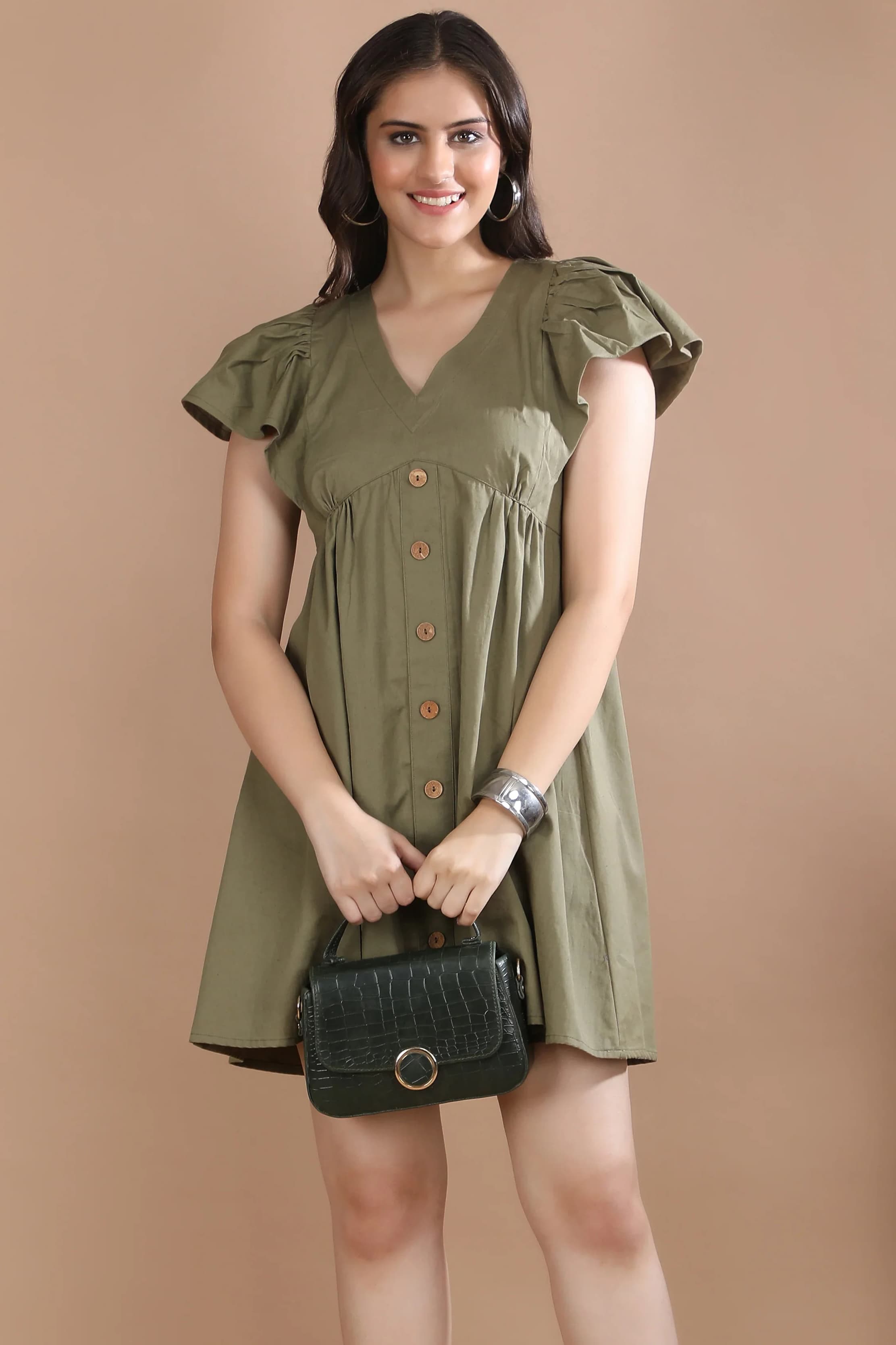 Front view of a woman wearing the premium olive green A-line dress with flutter sleeves by Guilt & Class, styled with brown heels and a green handbag.