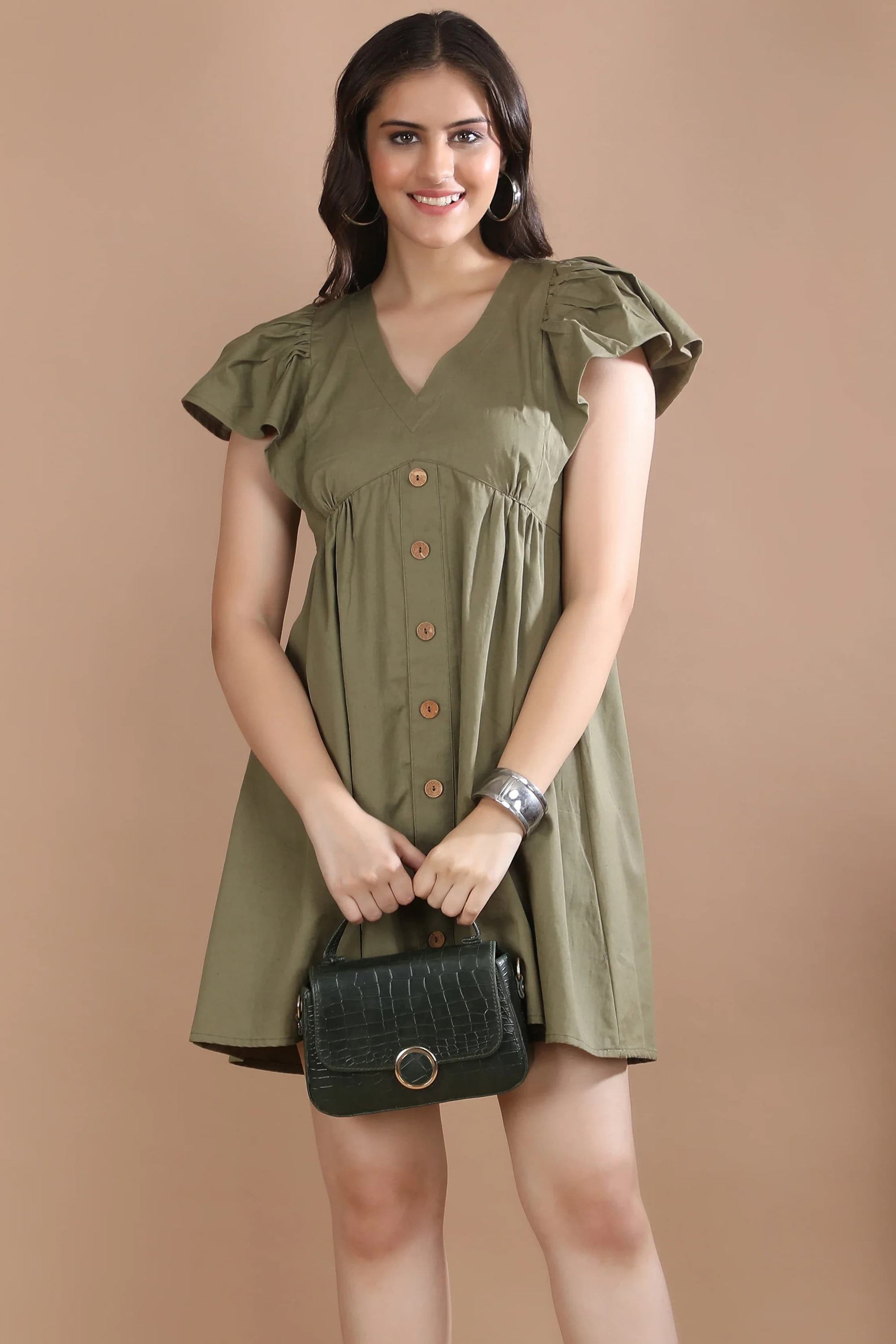 Front view of a woman wearing the premium olive green A-line dress with flutter sleeves by Guilt & Class, styled with brown heels and a green handbag.