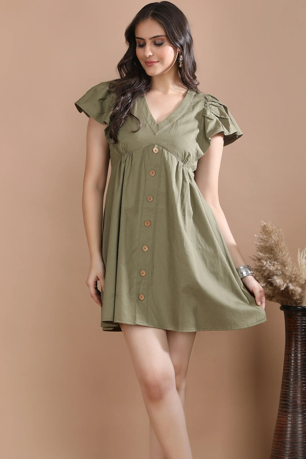 A model gently holding the hem of the olive green cotton twill dress, demonstrating the lightweight movement and premium drape of the fabric.