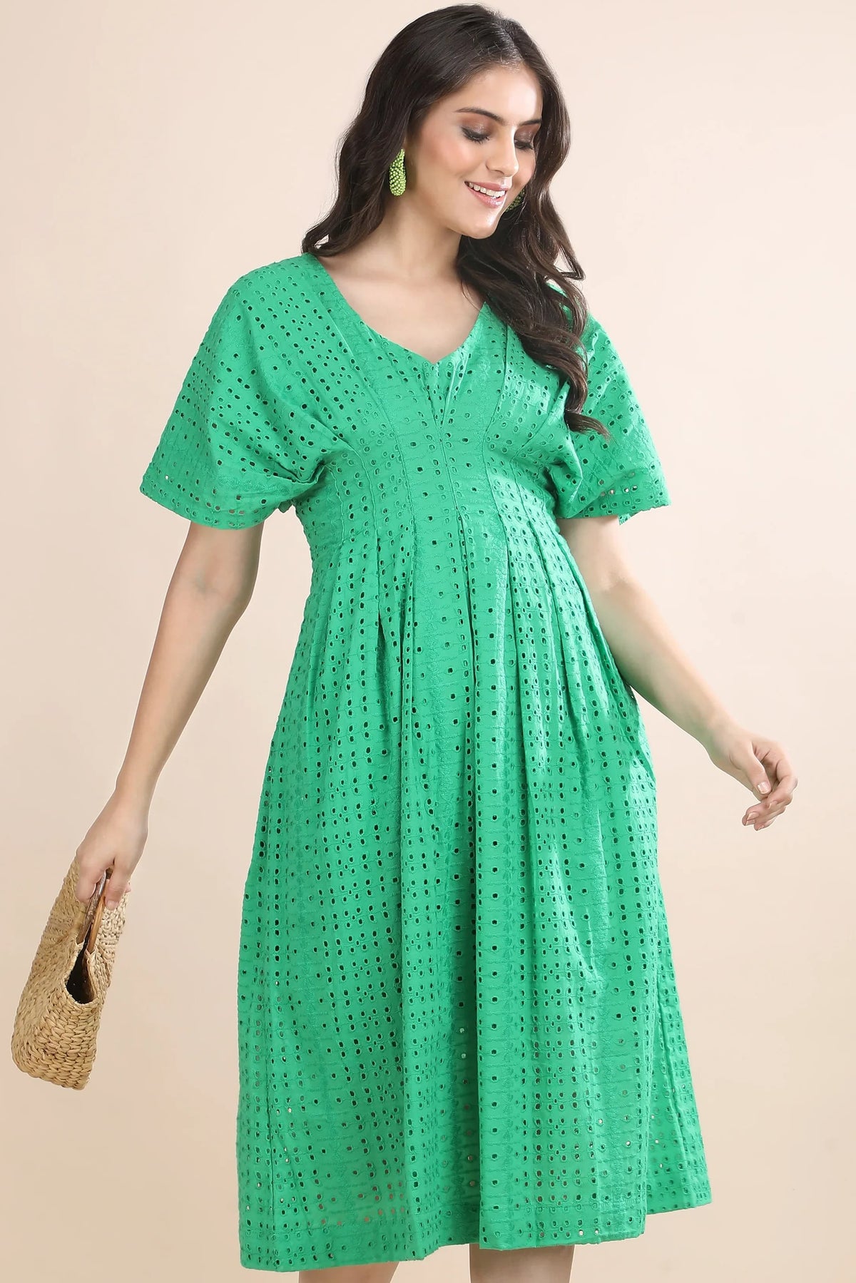 A model walking in the Whisper of Schiffli green midi dress by Guilt & Class, styled with a woven straw bag for a premium summer look.