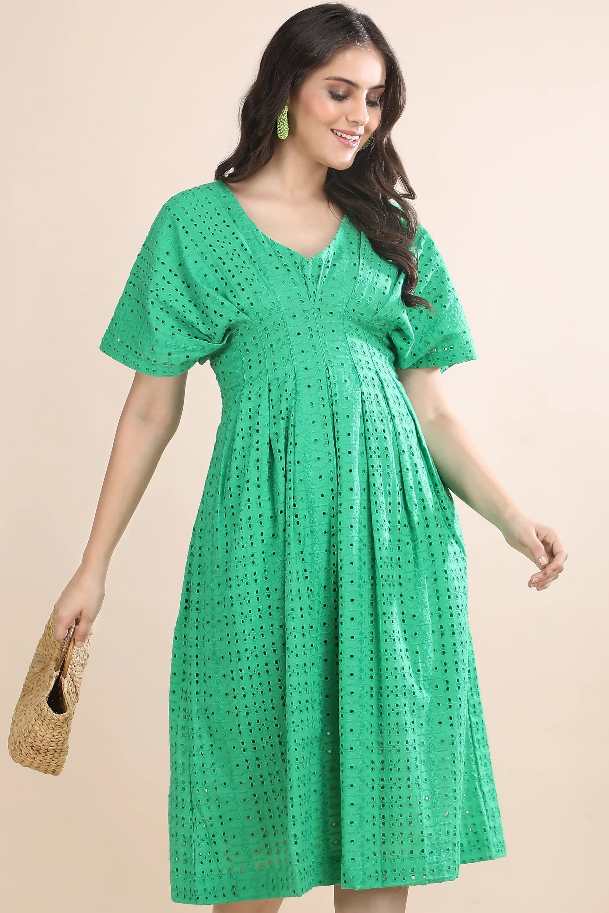 A model walking in the Whisper of Schiffli green midi dress by Guilt & Class, styled with a woven straw bag for a premium summer look.